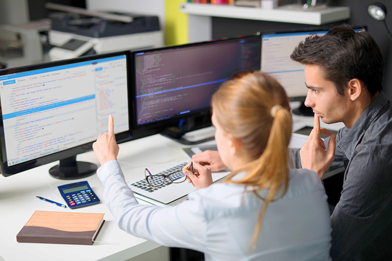 Symbolbild zum Jobprofil Softwareentwicklung: Zwei Beschäftigte schauen sich auf dem Bildschirm einen HTML-Code an.